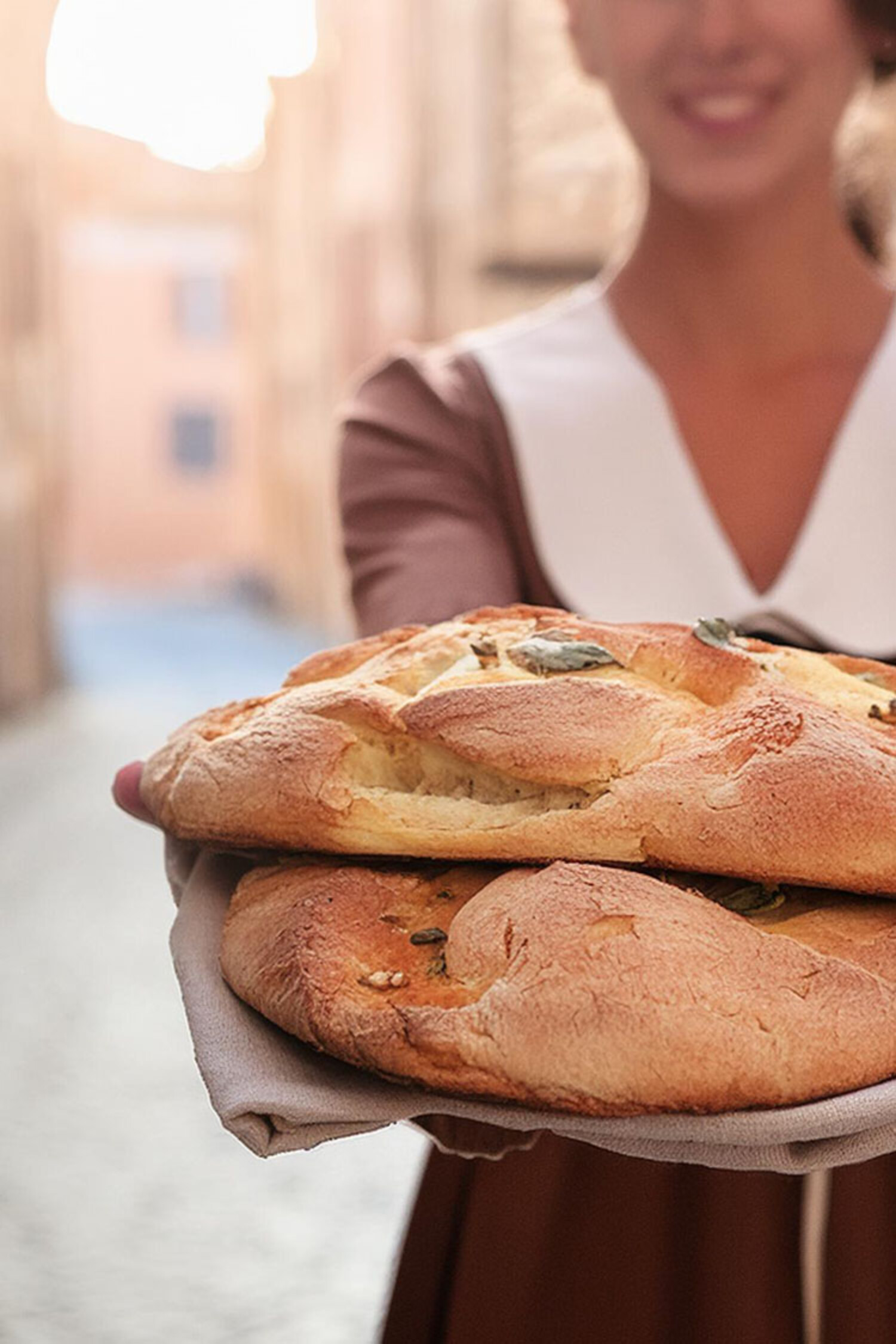 Hintergrundbild für Corporate Design von Bäckerei il Panetto zeigt eine Frau auf Straßen von Italien mit Lächeln und frischgebackenem Brot